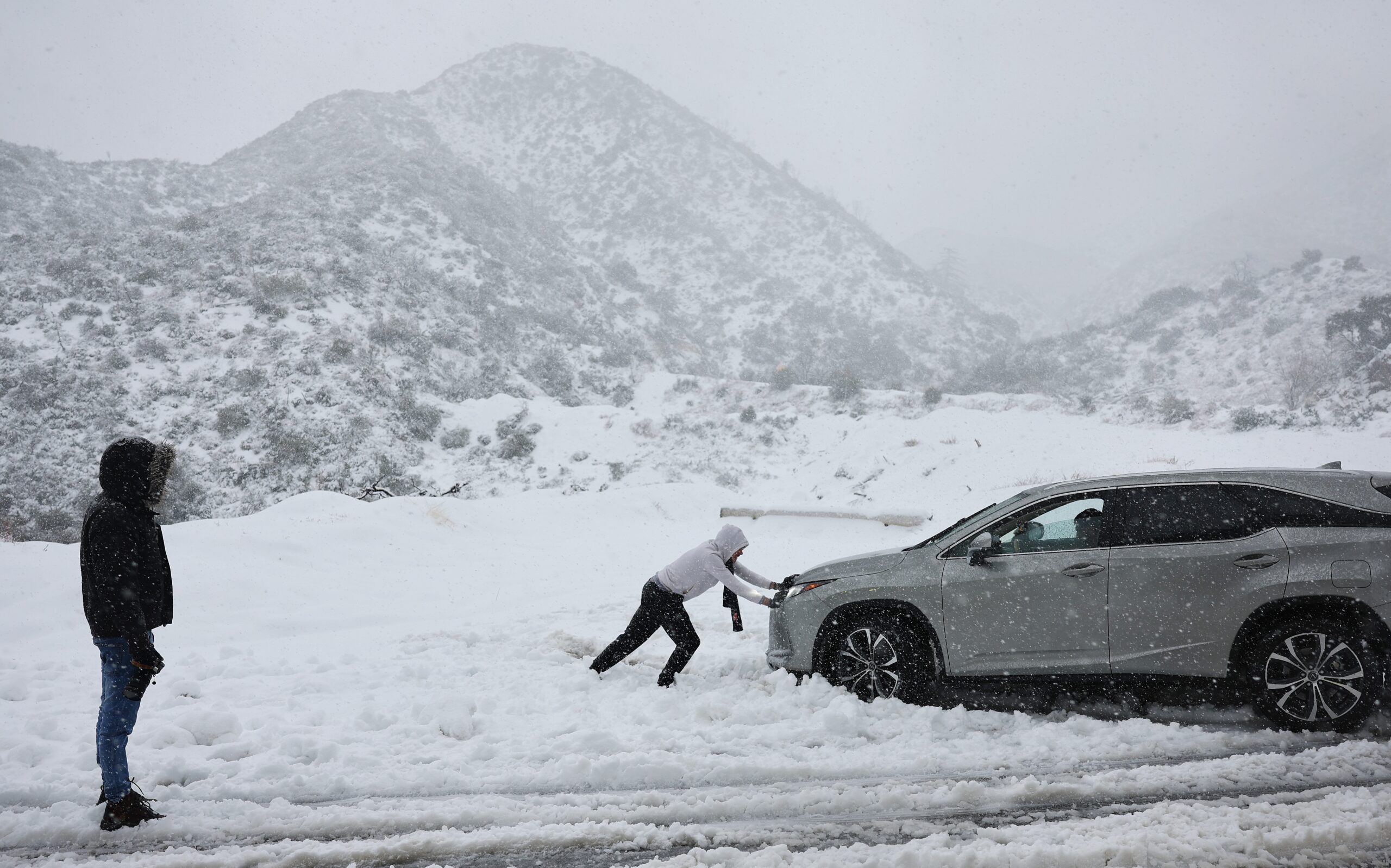 LA CANADA FLINTRIDGE, CALIFORNIA - FEBRUARY 24: A person helps push out a car that became stuck in ...