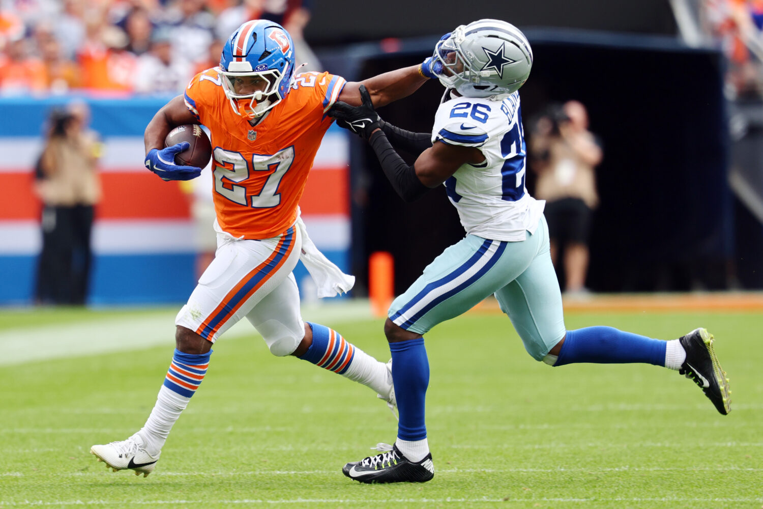 DENVER, COLORADO - OCTOBER 26: J.K. Dobbins #27 of the Denver Broncos stiff arms DaRon Bland #26 of...
